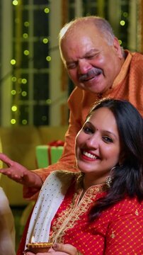 Wishing happy Diwali to camera, Indian family of four including senior mother in saree, father, young girl, husband sitting indoors with festive diya and rangoli celebrating Hindu festival together