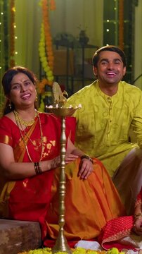 Wishing happy Diwali to camera, Indian family of four including senior mother in saree, father, young girl, husband sitting indoors with festive diya and rangoli celebrating Hindu festival together