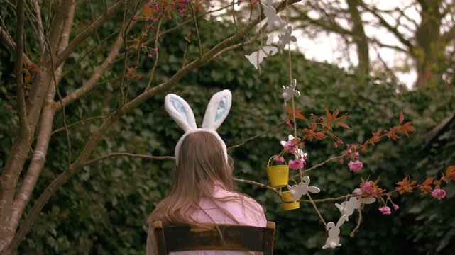 Woman wearing Easter bunny ears sits by easter decorations on blossom tree