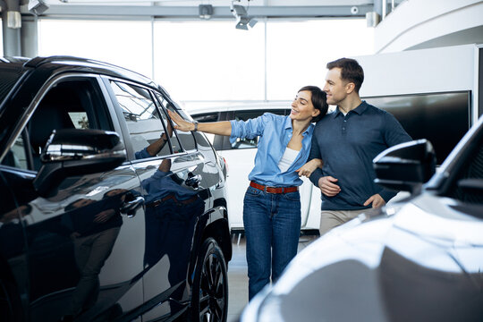 Happy couple embracing, looking at new vehicle in a car dealership, making a purchasing decision for an automobile