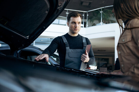 Car mechanic in uniform holding clipboard, discussing vehicle maintenance plan with female client at an auto service station