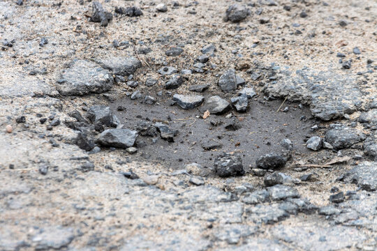 La Tuque, Canada, 01 May 2026 : A close-up view of a damaged asphalt road with a pothole filled with water and loose gravel.