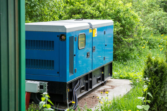 Hi-tech modern electric generator device standing outdoors at backyard near residential house, independent power station delivering stable consistent electricity, generator placed outside of building.