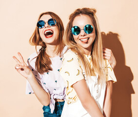 Two young beautiful smiling blond hipster in trendy summer colorful T-shirt clothes. Sexy carefree...