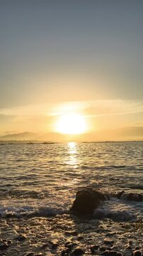 Slow motion of golden sunrise over a calm tropical sea with gentle waves washing ashore on a rocky beach. Papuma Beach, Jember, Indonesia.