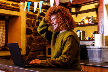 Obraz premium Redhead woman laughing while working on laptop, enjoying remote connection from rustic home