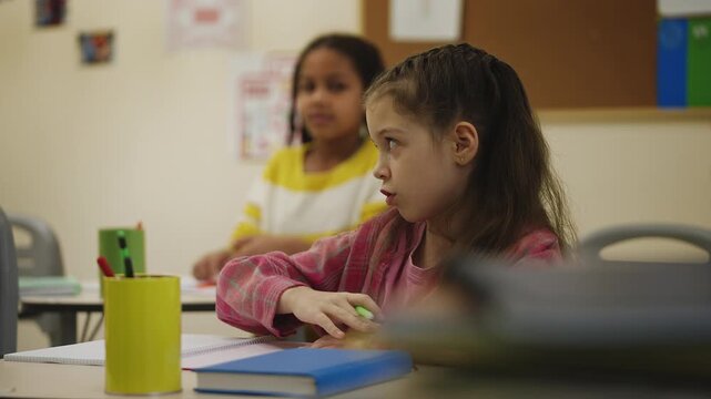 Schoolgirl raising hand to answer teacher's question during classroom lesson