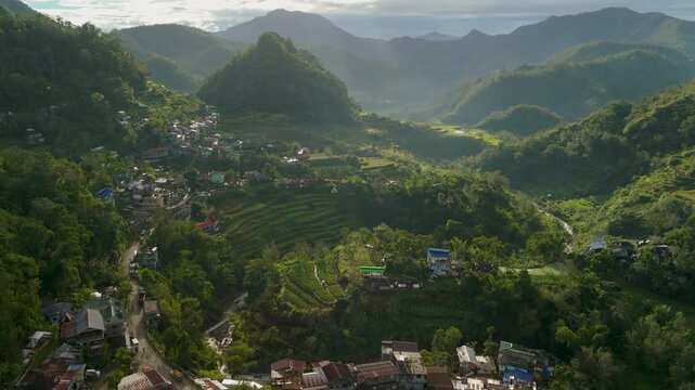 Aerial flypass over Banaue cityscape ascends to reveal scenic rice terraces, garden plots and dramatic misty mountain panorama in morning light Ifugao Philippines