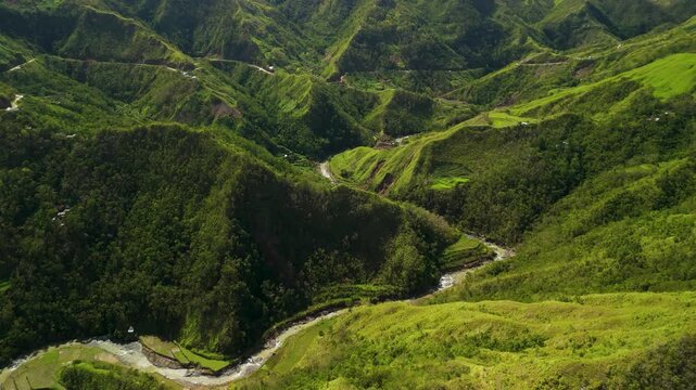 Aerial slow forward reveals the sinuous Ducligan Snake River winding through a lush forested mountain gorge with switchback road and scattered terraces in Ifugao Philippines