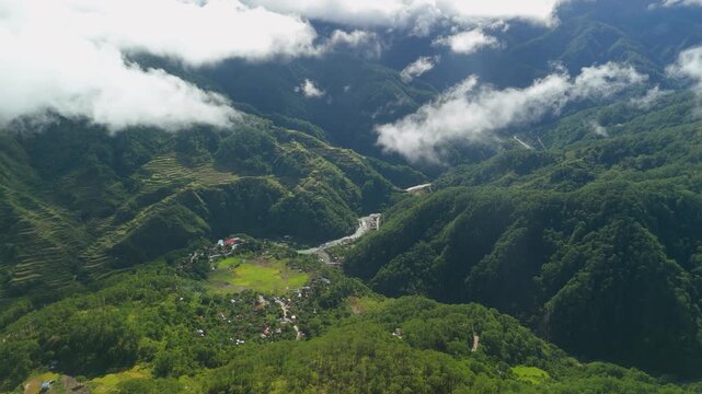 High-altitude parallax over Sagada Marlboro Hill reveals a dramatic deep forested valley with a remote village, rice terraces and low-hanging clouds in Philippines