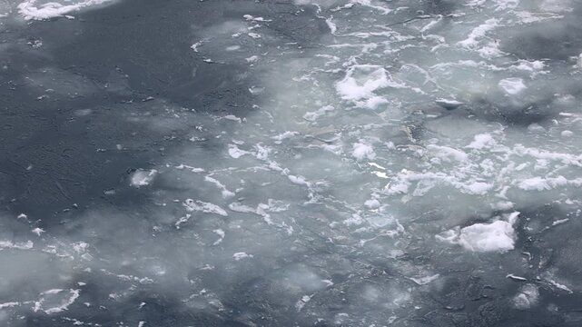 Thin Antarctic sea ice fragments drift across dark polar water beside an expedition ship bow in the Southern Ocean, elevated observational shot from ship bow above fractured marine ice surface.
