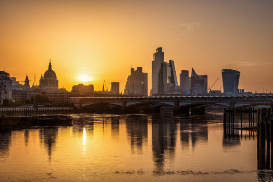 Golden summer sunrise view of the skyline of the City of London, England, with reflections in the River Thames