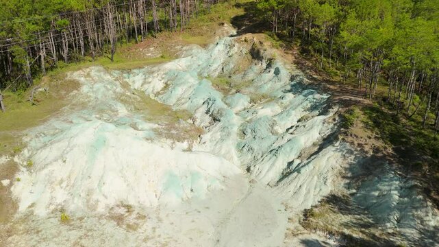 Slow ascending aerial shot rises above Sagada Blue Soil Hills revealing white-blue clay formation and dirt trail cutting through pine forest in Mountain Province Philippines