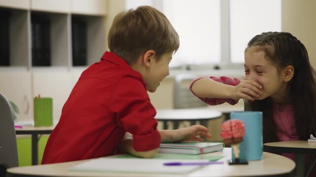 Smiling schoolchildren laughing and talking during boring classroom lesson