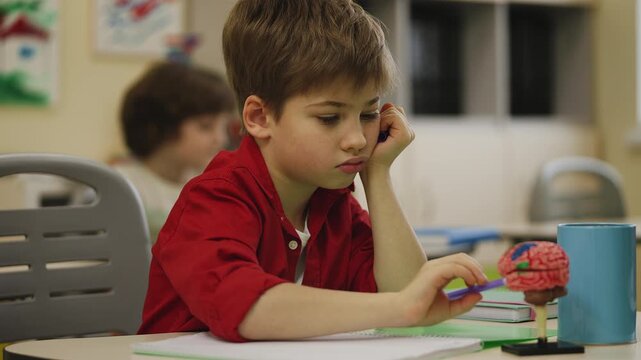 Tired primary school boy playing and not paying attention during boring lesson