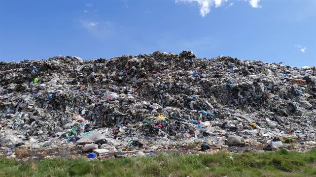 Waste and garbage fill the landfill area under a clear sky. Items are mixed together as far as the eye can see