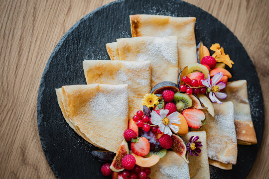 Stack of pancakes and fluffy fritters served on a plate, topped with fresh berries and fruit. Delicious homemade breakfast or brunch with a healthy and colorful presentation.