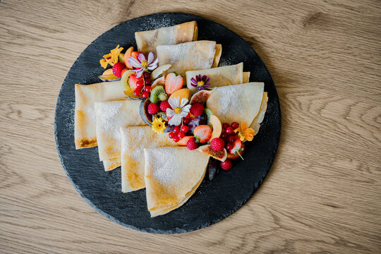 Stack of pancakes and fluffy fritters served on a plate, topped with fresh berries and fruit. Delicious homemade breakfast or brunch with a healthy and colorful presentation.
