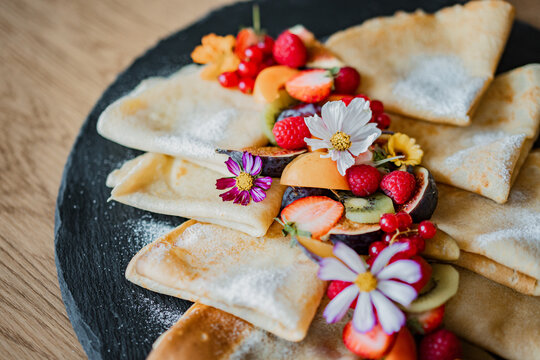 Stack of pancakes and fluffy fritters served on a plate, topped with fresh berries and fruit. Delicious homemade breakfast or brunch with a healthy and colorful presentation.