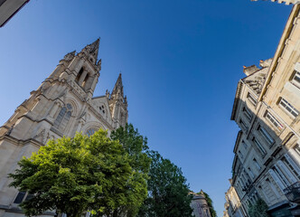 Saint-Louis Church rises above the trees in Quartier des Chartrons, Bordeaux. The church features tall spires and intricate details on its stone facade. The clear sky adds to its presence. © FreeProd