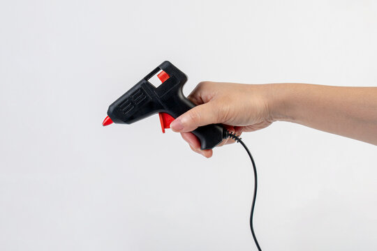 Electric hot thermal melt glue gun for DIY craft work and hand on white background.