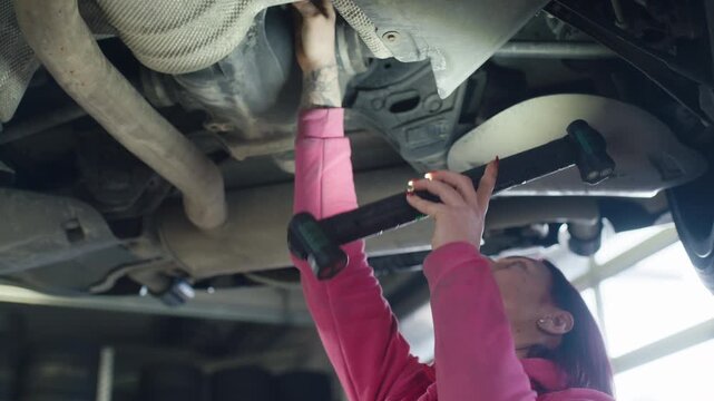 a professional female auto mechanic using a torch to inspect an undercarriage on the lifted vehicle