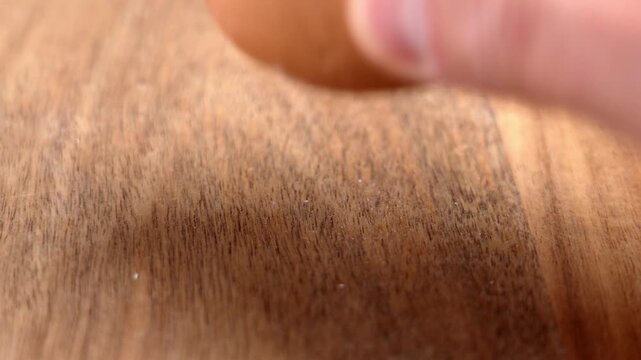 Close-up of a human hand tapping and cracking a brown boiled egg against a wooden table surface to peel the shell