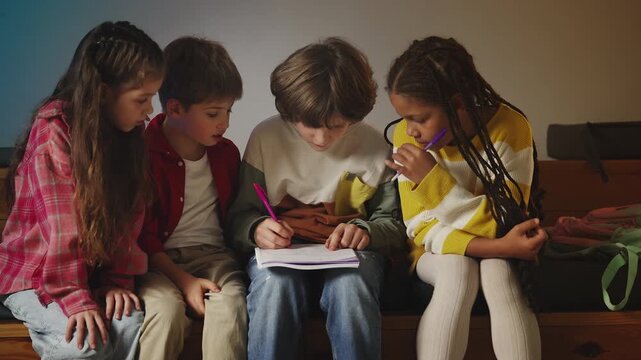 Focused schoolchildren solving math equations and writing in notebook together