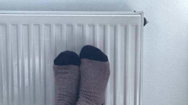 Women's feet in warm socks on the radiator. The atmosphere of home comfort, relaxation and comfort, enjoying a good temperature in the apartment during the cold winter period