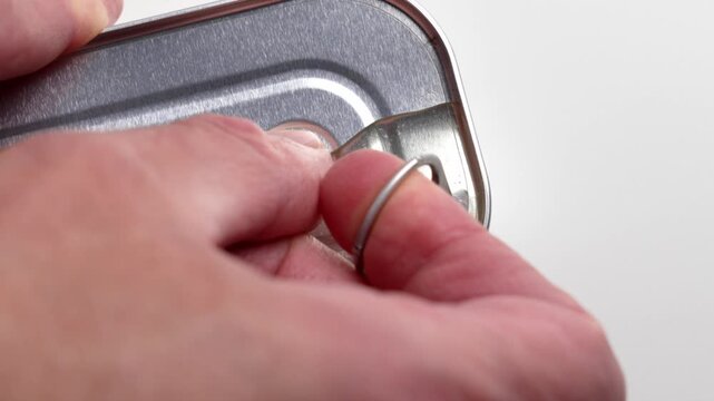 Closeup of human hand opening a metal can with cod liver in oil using pull tab lid mechanism. Canned seafood product.
