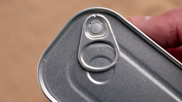 Closed silver tin can of cod liver on a brown background held by a hand. Metal container equipped with an easy-open pull tab ring
