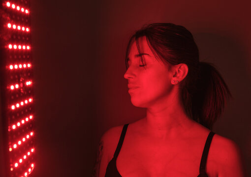 Young woman receiving red light therapy treatment from an led panel, promoting skincare and anti-aging