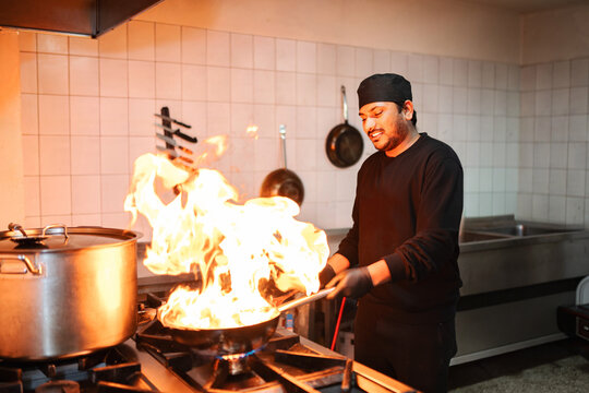Male chef flambe cooking food in a pan on a stove