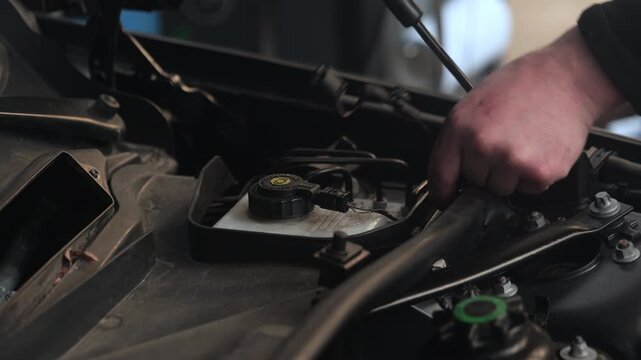 Unplugging a connector under the hood of a car. Close up hands and engine compartment.