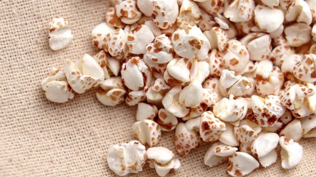 Puffed buckwheat grains scattered on rustic burlap fabric background. Organic gluten free cereal. Rotation