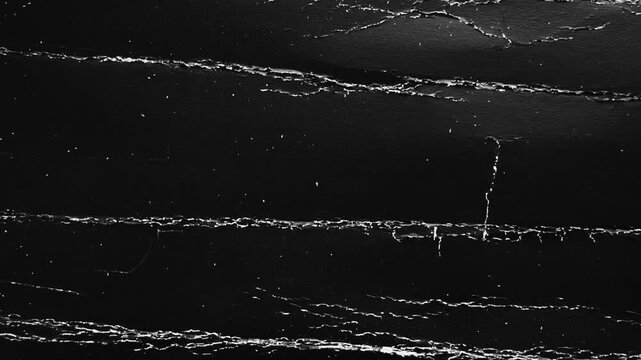 Moving abstract black grunge texture with white cracked folds. Dark monochrome background featuring a worn surface. Distressed wrinkles and wrapping cardboard defects