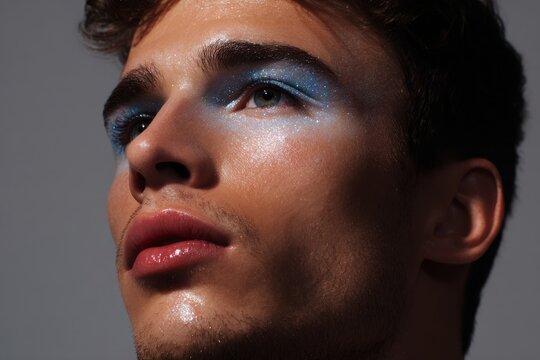 Trend male close up portrait with shimmering sky blue eye shadow and radiant cheek highlight for fashion editorial banner