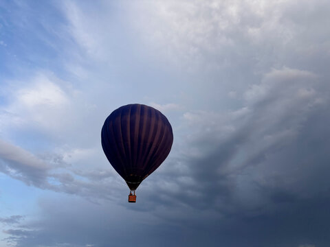 Dark Purple Hot Air Balloon Floating in Dramatic Cloudy Sky at Sunset