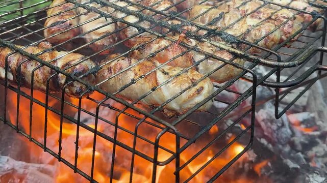 Crispy bacon wrapped sausages grilling on metal grate above hot fire during outdoor picnic cooking with cozy barbecue atmosphere in nature.