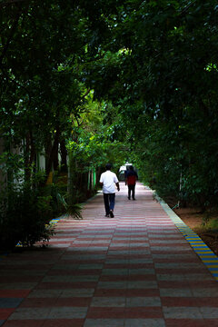 Two people walk down a shaded, tiled path