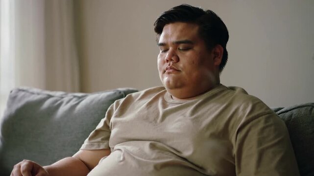 Diffused sunlight lulling adult Asian man closing eyes on couch at home, with white mug