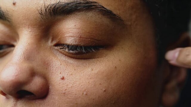 Approaching light-toned finger pressing closed right eyelid in close-up, revealing mole and pores