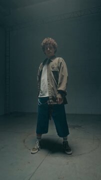 Vertical shot of young man entering shot and dancing dynamic hip hop choreography facing camera in studio lit by flashing lights, social media story format