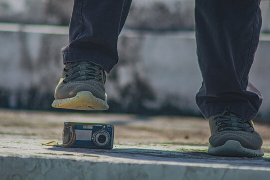 Unrecognizable man about to crush digital camera with his foot outdoors