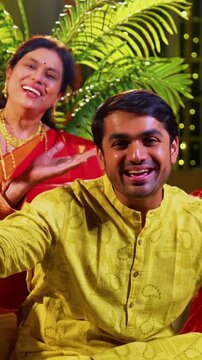 Wishing happy Diwali to camera, Indian family with young daughter, senior mother in saree, father an husband in traditional wear sitting on indoor steps decorated with diya, rangoli, smiling joyfully
