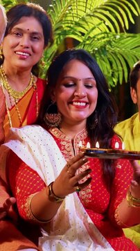 Wishing happy Diwali to camera, Indian family with young daughter, senior mother in saree, father an husband in traditional wear sitting on indoor steps decorated with diya, rangoli, smiling joyfully