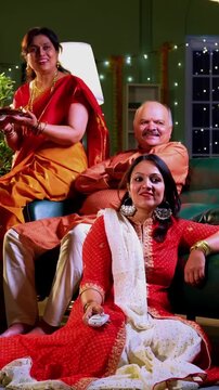 Son seeking Diwali blessings from parents, Indian family in festive home with senior mother in saree, father, and young daughter watching funny show on TV together after son greets with warm gesture