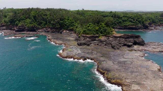Aerial drone footage of the scenic rocky headland near Batangang Cape, Quang Ngai, Vietnam. The green tropical vegetation-covered cliffs meet the turquoise South China Sea in this dramatic coastal lan
