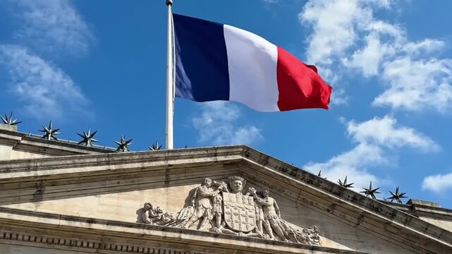 French flag flying over a historic stone building with a sculpted pediment