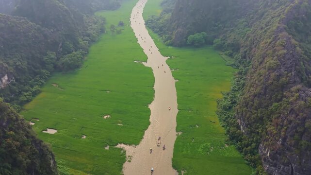 Cinematic tilt up drone reveal of the Trang An river waterway with tour boats traveling through towering limestone karsts in Ninh Binh, Vietnam.